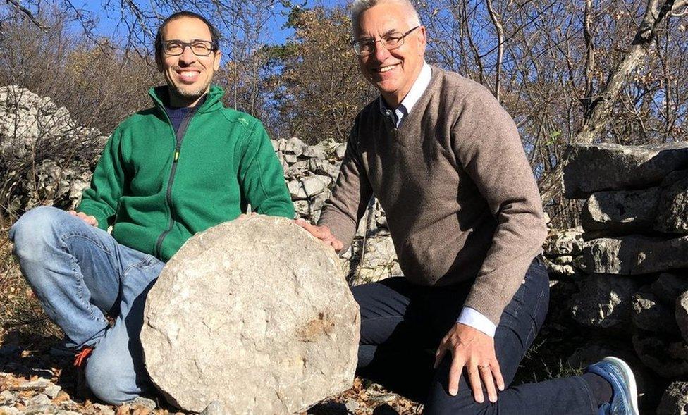 two men posing with the stone disc outside