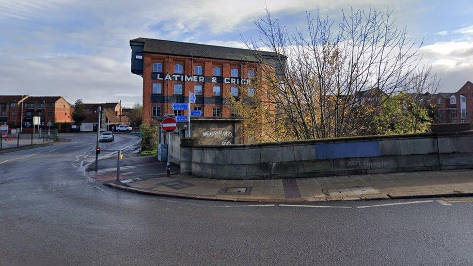 Road sweeps by old toilet building and old factory.