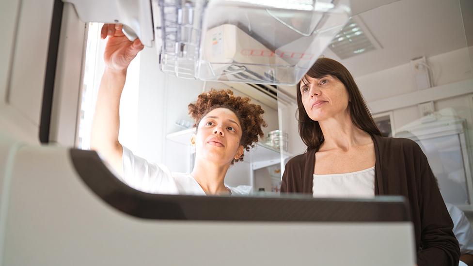 A healthcare professional and a patient discuss mammography results as they stand behind a scanner