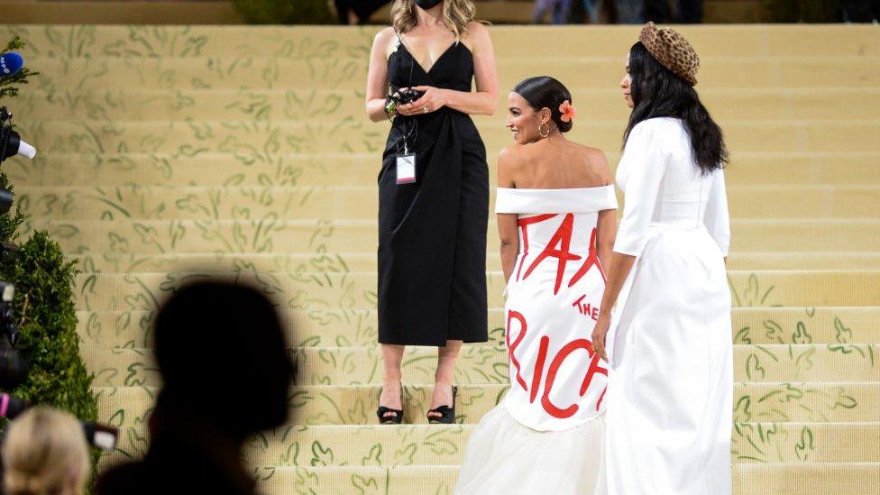 Alexandra Ocasio-Cortez wearing a white formal dress with the words "Tax the Rich" scrawled in red on the back