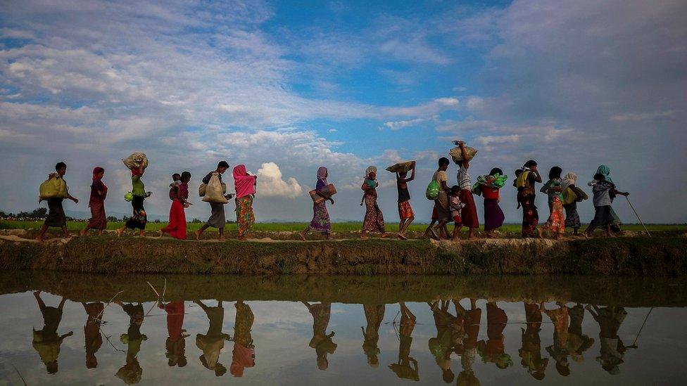 Rohingya refugees walking along a lakeside in Bangladesh