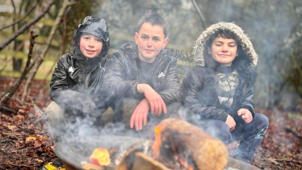 Youngsters Bertie, Vinnie and Harrison sat by a fire pit