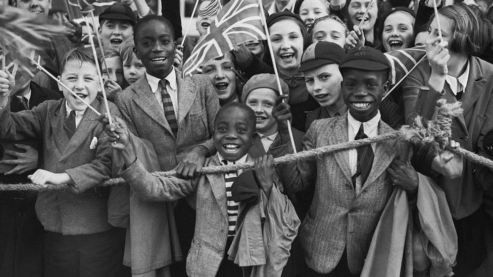 Children line up in Brixton waving union jacks as Queen Mary visits to open Lambeth Town Hall, 1938