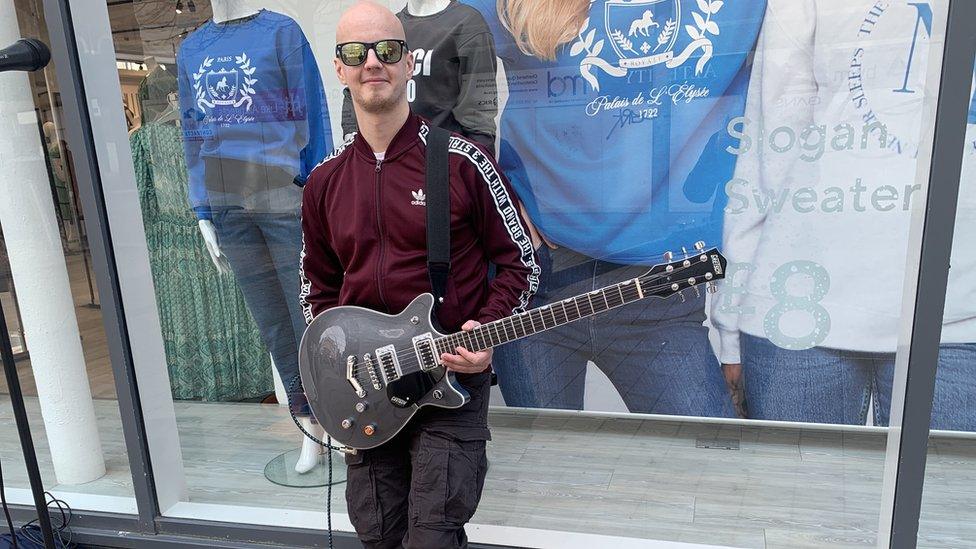 Busker Deano White poses with his guitar outside a shop window in Belfast city centre