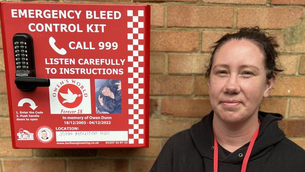 The first bleed control kit installed by Owen's World fixed to Penhill's community hall wall with CEO Joanne Davis stood next to it