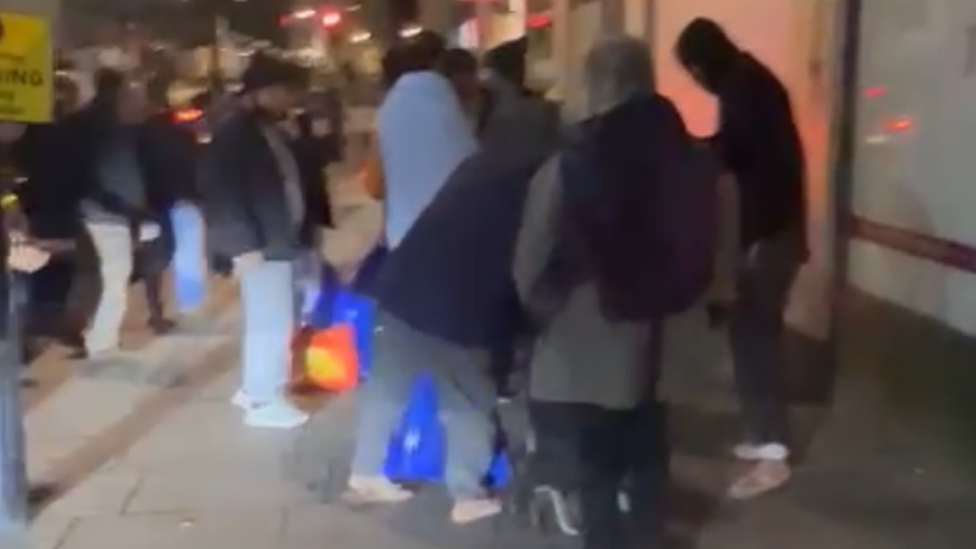 The group of migrants pictured waiting for taxis to take them to Norwich after being left stranded in London