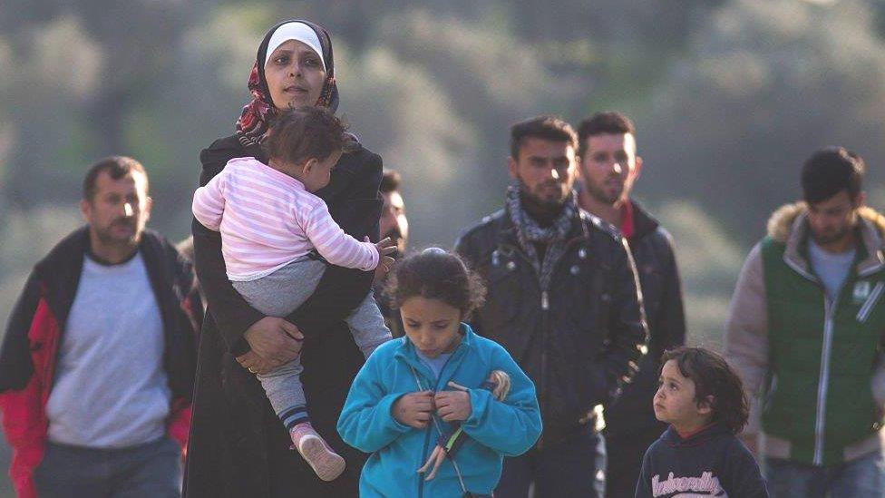 Refugee and migrant families walk through the Moria Refugee Camp in 2016