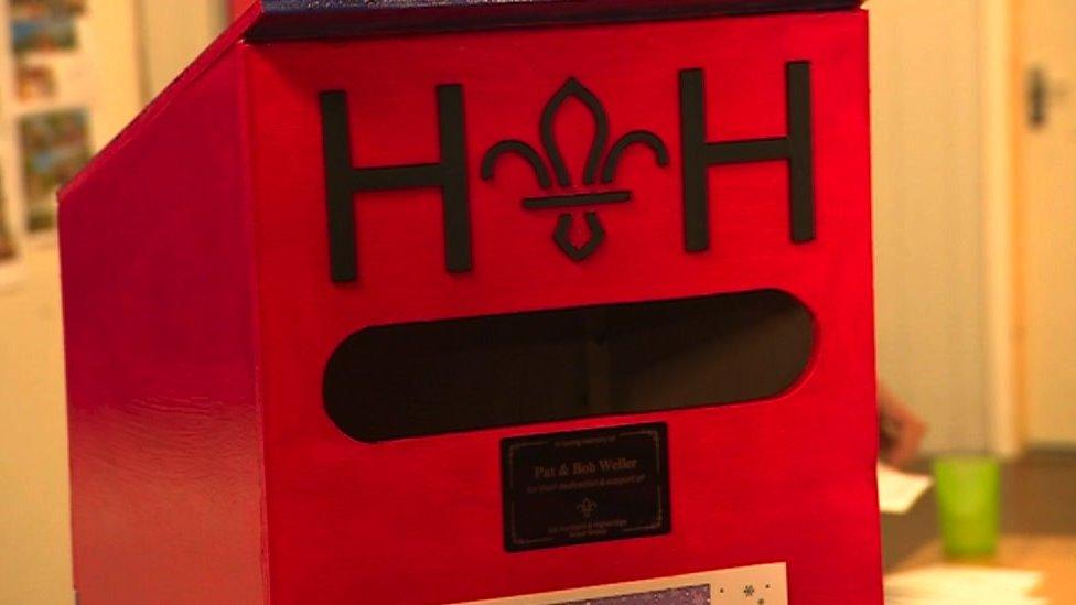 Scout Post box. It is a red box with HH at the top in black letters. Below the letter slot, there is a small plaque reading 'Pat and Bob Weller'