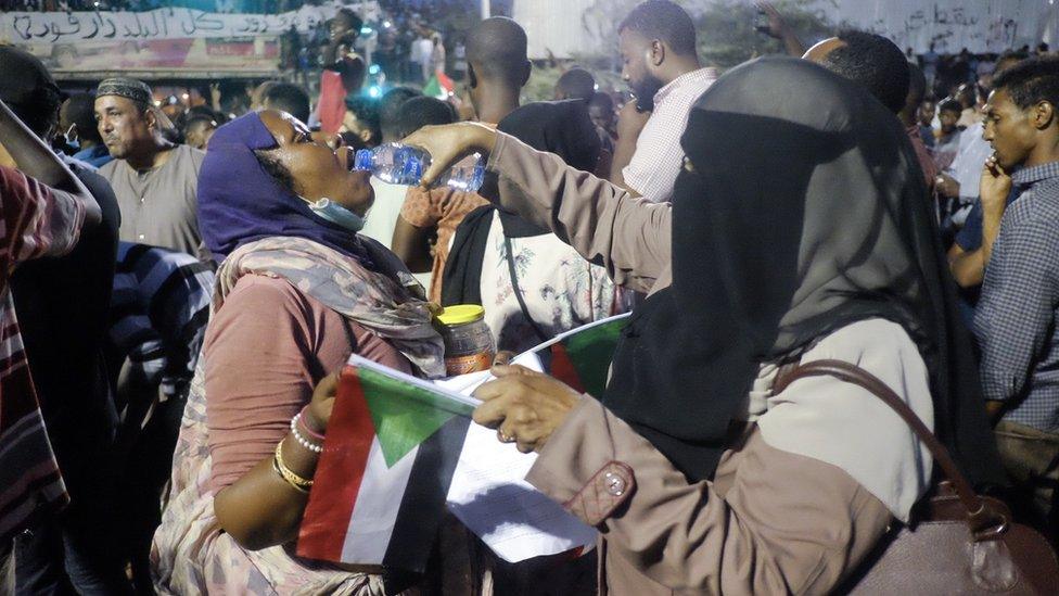 A woman wearing a headscarf and face veil pours water into the mouth of another protester at a sit-in at the military HQ in Khartoum, Sudan - Sunday 7 April 2019