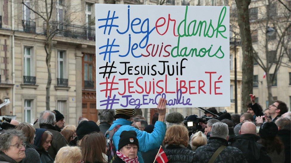 A man holds a placard with the hashtags 'I am Danish, I am Jewish, I am Freedom' next to a woman holding a Danish flag outside the Danish Embassy in Paris