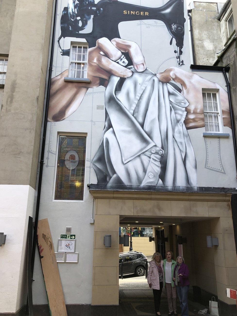 factory girls standing under mural