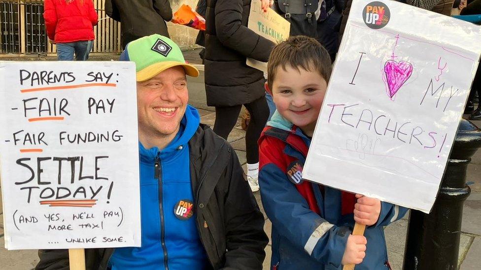 A man and boy with placards supporting teachers