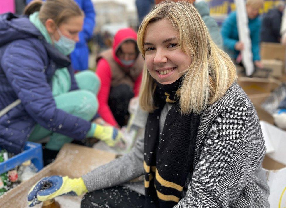 Arina sits with other women, preparing Molotov cocktails. She is dusted with white polystyrene chunks that are a component of the bottle-bombs