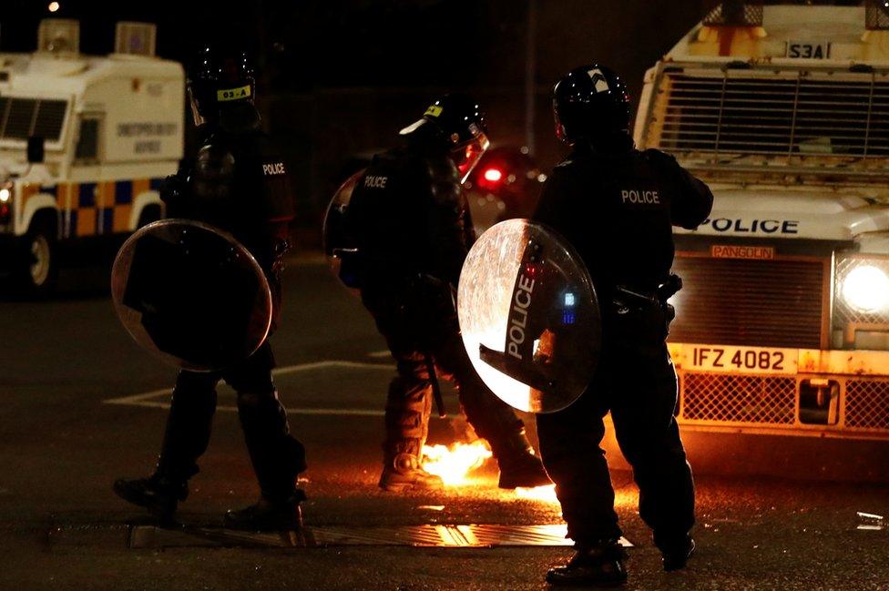 Police in riot gear watch as a petrol bomb lands close to them in Belfast