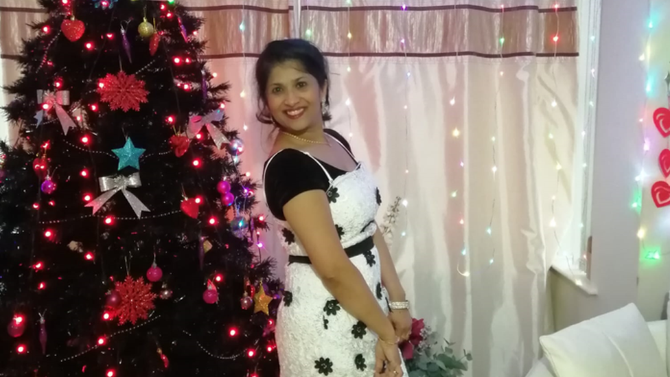 A woman stands in front of a Christmas tree in a room decorated with Christmas lights