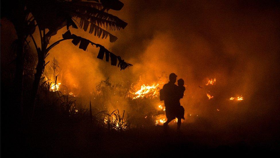 A man and child walk past burning forests