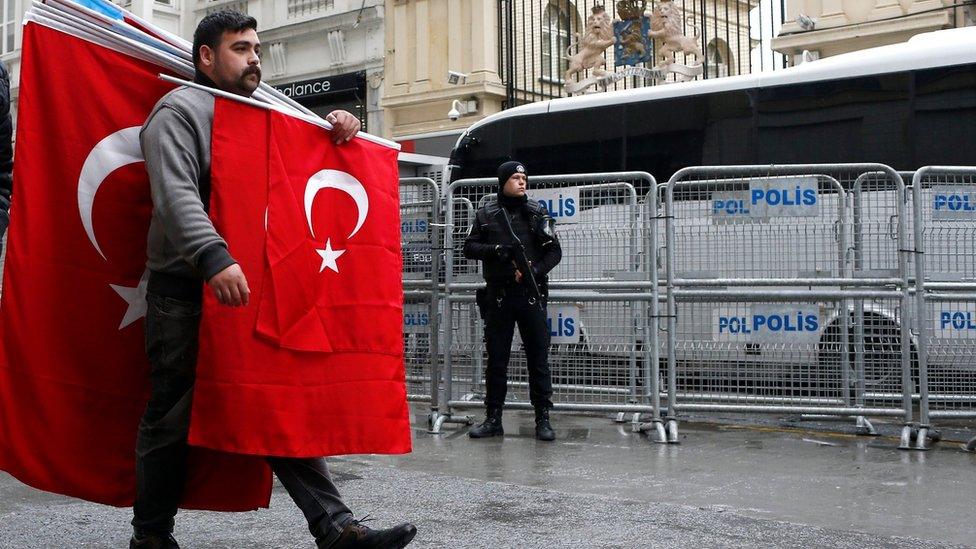 A man carrying Turkish flags walks past a Turkish armed riot policeman in front of the Dutch Consulate in Istanbul, Turkey, 13 March 2017.