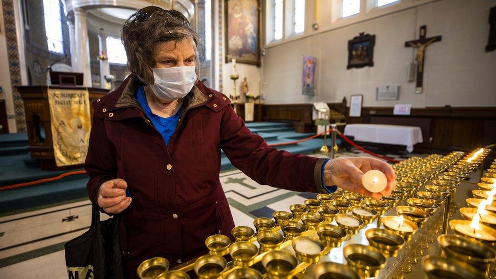 A woman wearing a face mask lights candles at a church in Northern Ireland