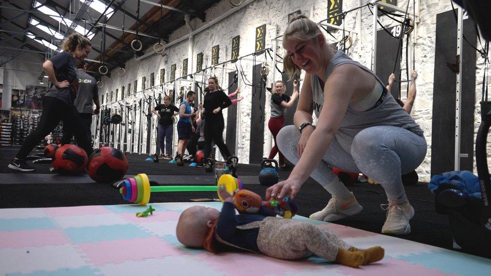 Vicky Aley crouched down next to baby on gym floor