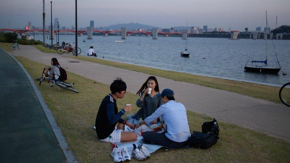 People sit on the grass alongside the Han river