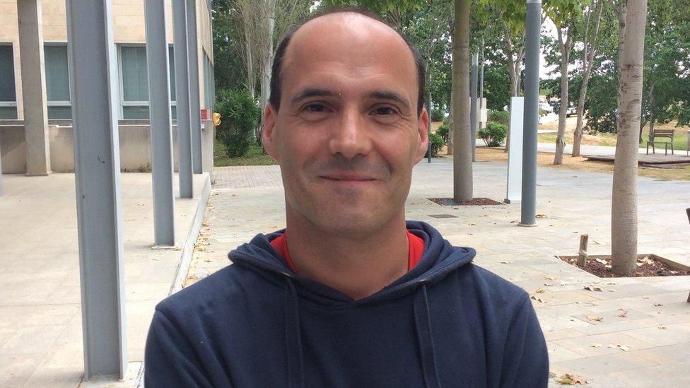 A bald man with some hair on the sides of his head smiling at the camera. He is young-looking.