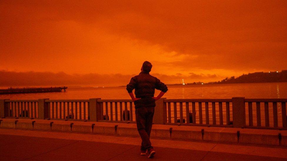 A man looks out towards the red orange sky across San Francisco.