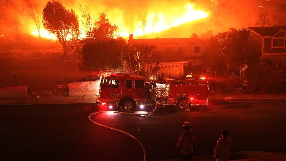 Los Angeles County firefighter looks on as the out of control Woolsey Fire explodes behind a house in the West Hills neighborhood