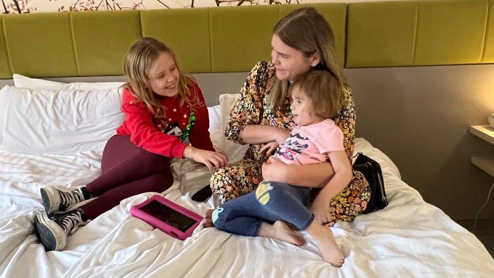 A mother with two girls sits on a double bed.