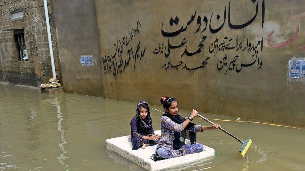 Girls use a temporary raft across a flooded street in a residential area after heavy monsoon rains in Karachi on July 26, 202