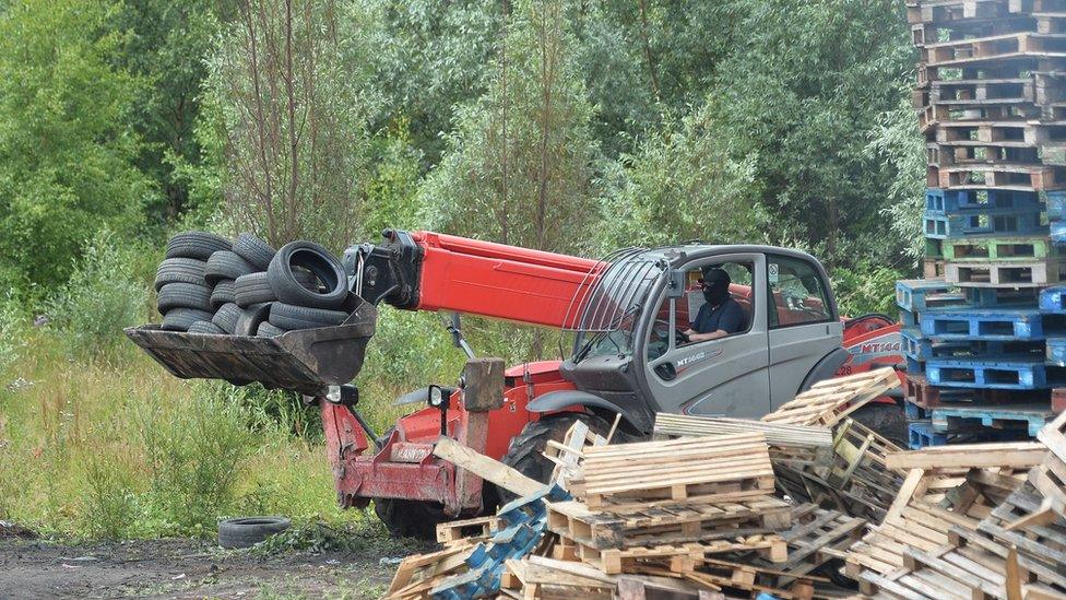 A man driving a telehandler removes tyres from the bonfire on London Road in Belfast