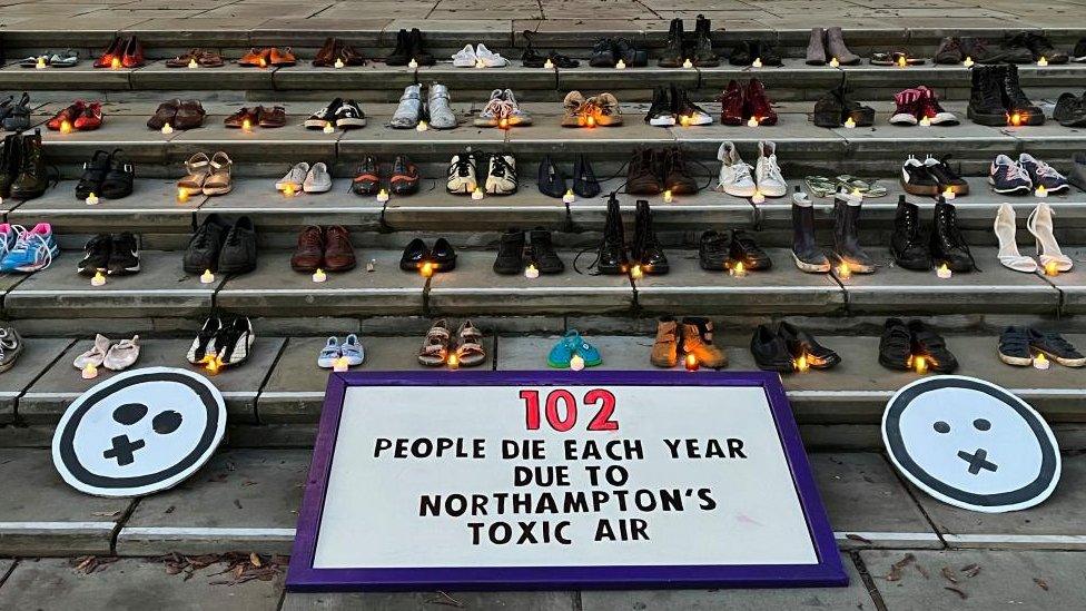 Different coloured pairs of shoes on stone steps, with a candle in front of each.