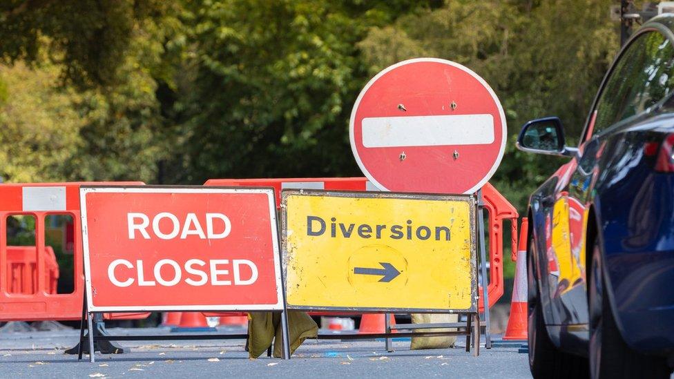 A red road closed sign next to a yellow diversion sign in a closed road