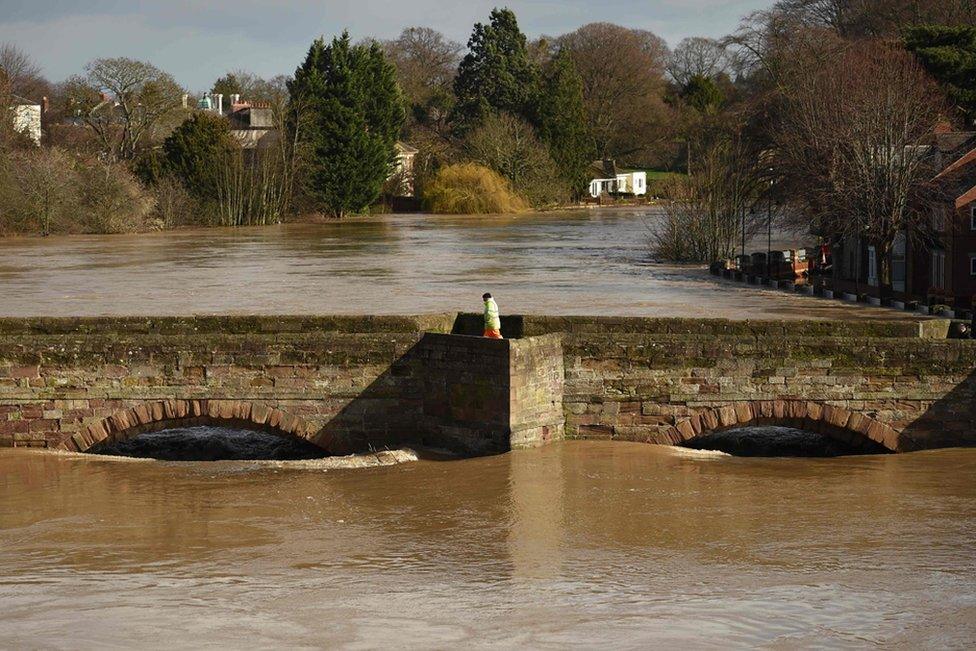 A man walks on the Old Bridge in Hereford as the waters of the swollen River Wye fill the arches