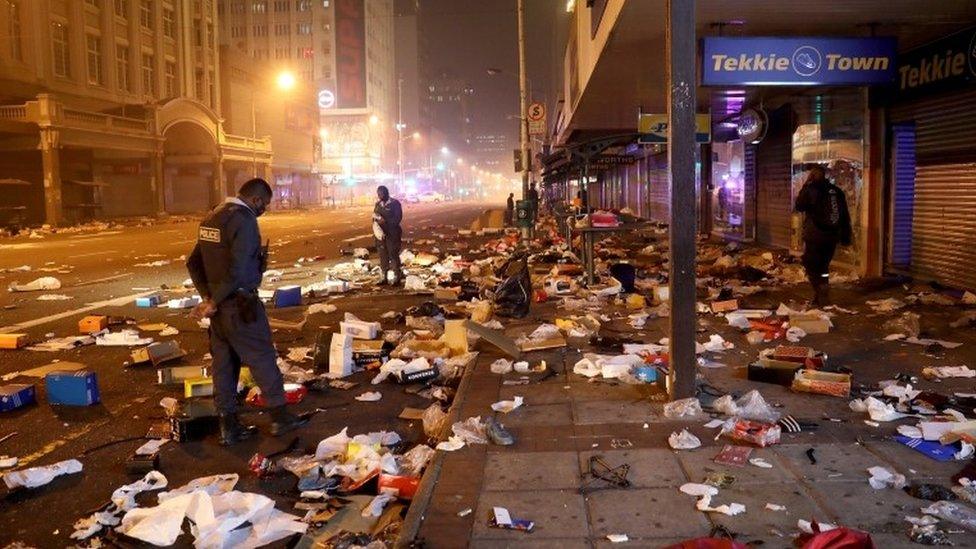 Police officers look at the remains of looted shops during protests in downtown Durban, South Africa, 12 July 2021