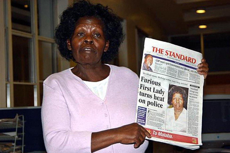 Pictured in May 2005, Kenya's First Lady Lucy Kibaki speaks to the media while holding a copy of a local newspaper with the headline 'Furious First Lady turns heat on police'