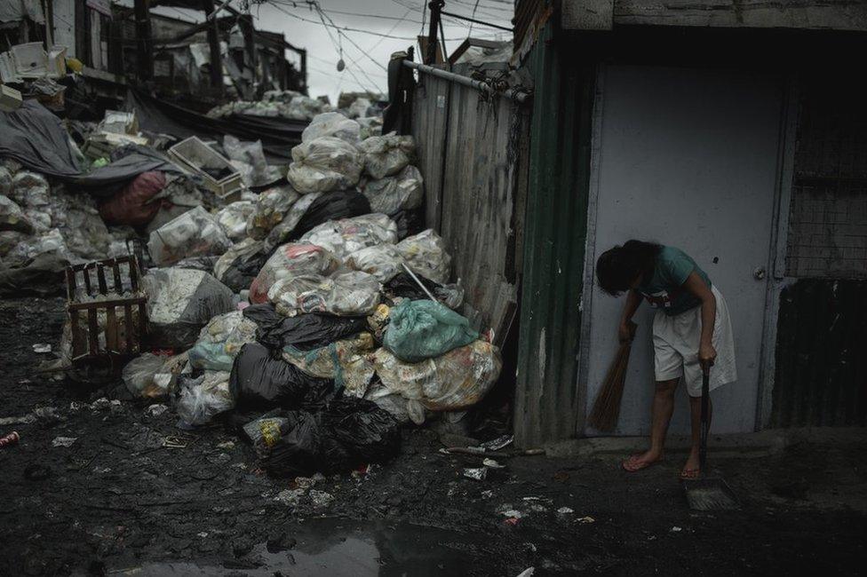 A woman sweeping the front of her house in Happyland a dump site in Tondo, Manila