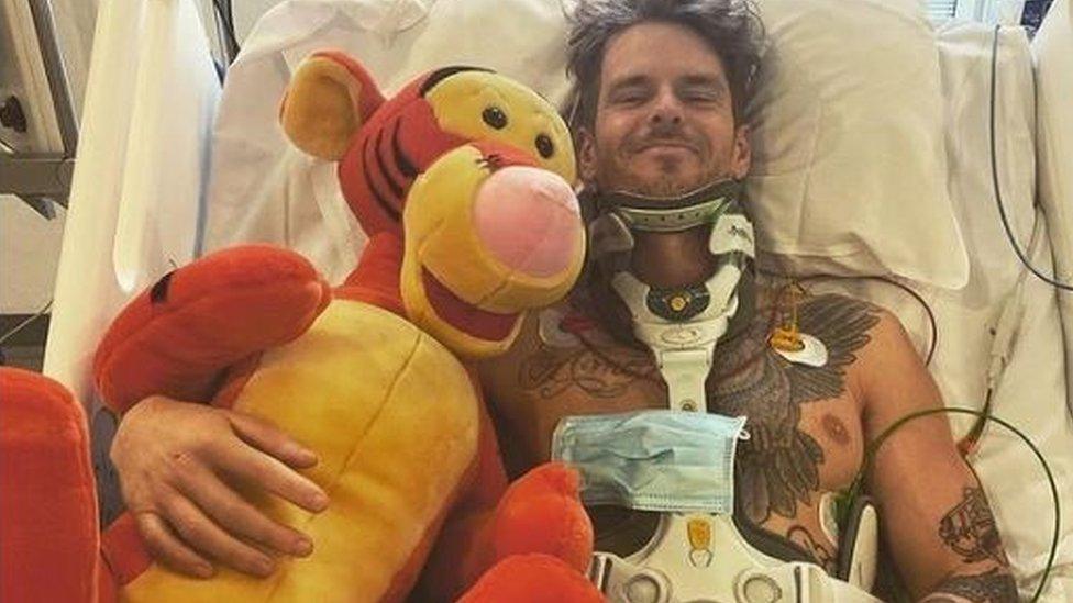 Will in a hospital bed hugging a large stuffed toy