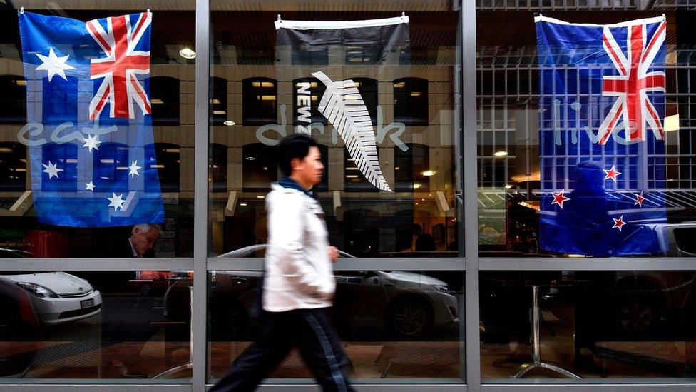 A man walks past the Australian flag, and two New Zealand flags hung up in the window of a bar