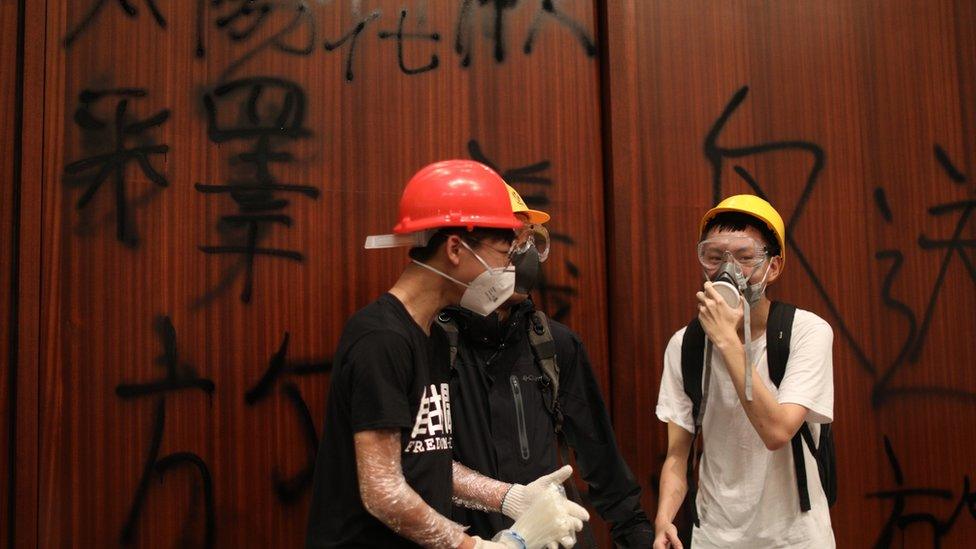 Protesters stand by a wall covered in graffiti