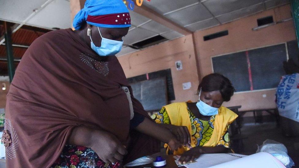 An official of Autonomous National Electoral Commission (CENA) tends to a voter at a polling station during the Benin Presidential election in Cotonou on April 11, 2021.