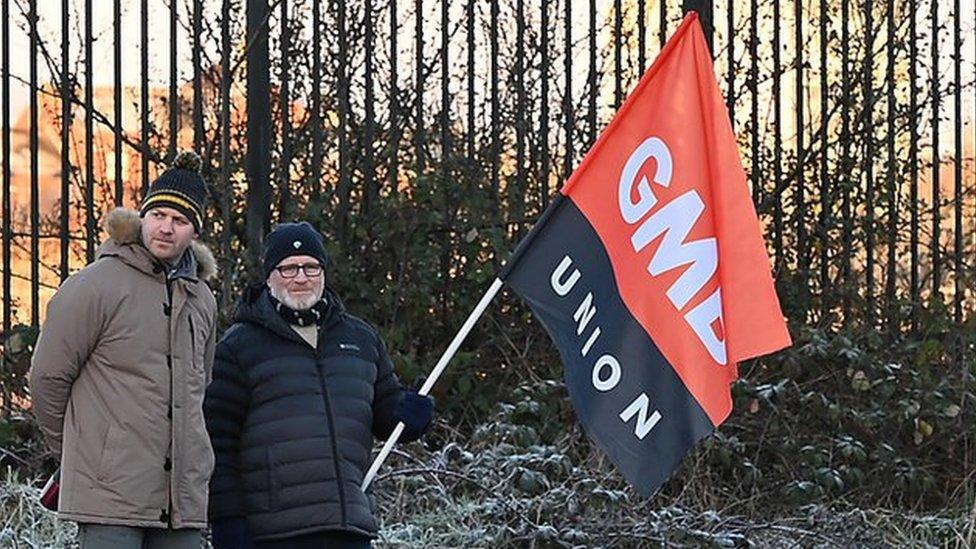 Two men on a picket line, one holding a GMB flag