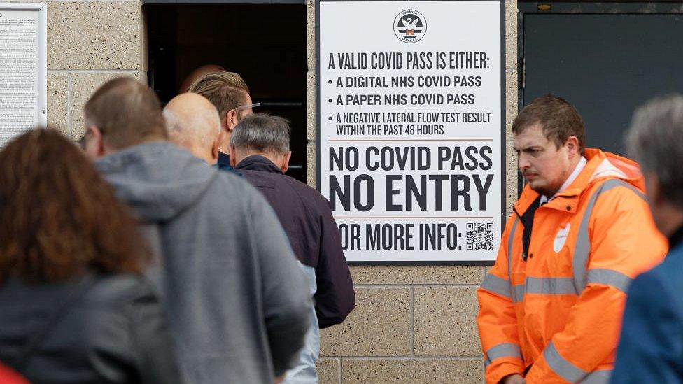 People queue into football stadium by sign reading 'no covid pass, no entry'