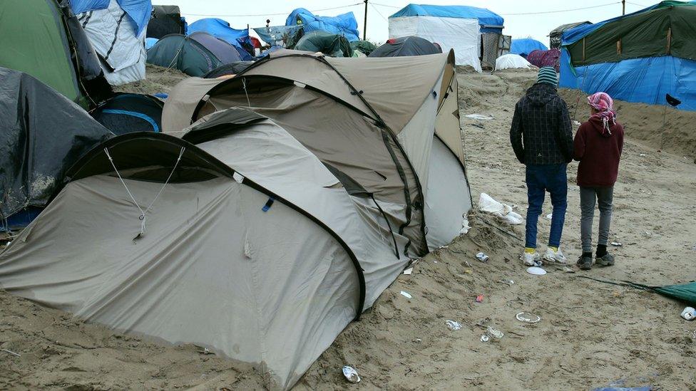 Orphaned children walk along muddy pathways between tents in the camp