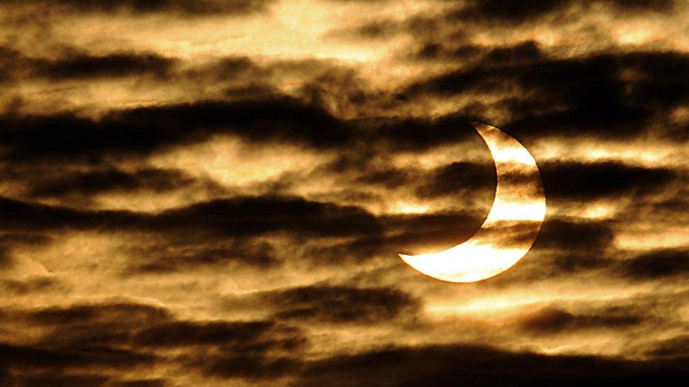 a crescent shaped sun in the sky covered by clouds