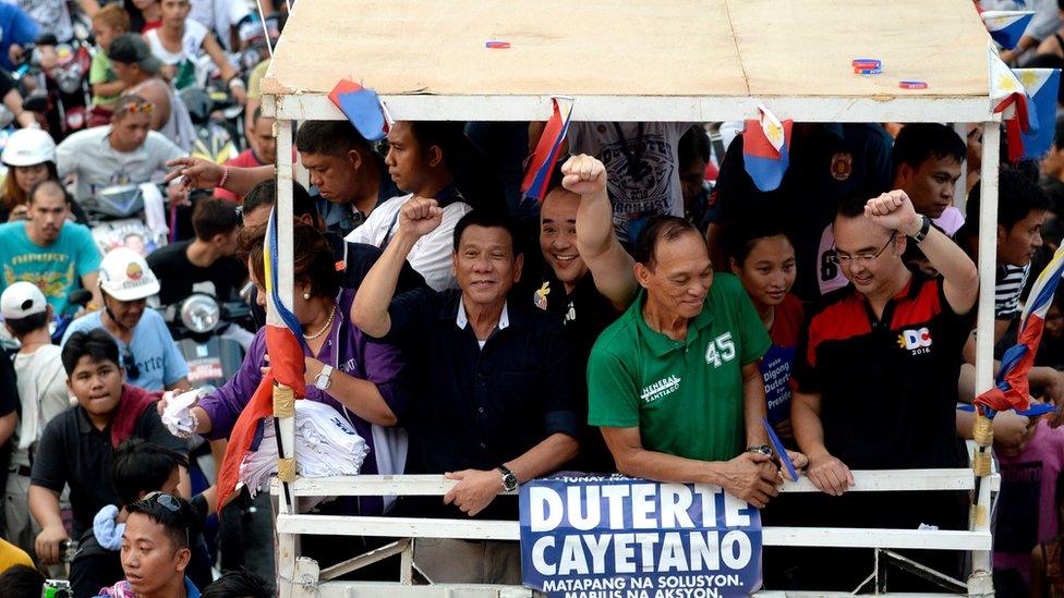 Rodrigo Duterte (centre, in black) gestures to the crowd from the top of a packed campaign bus