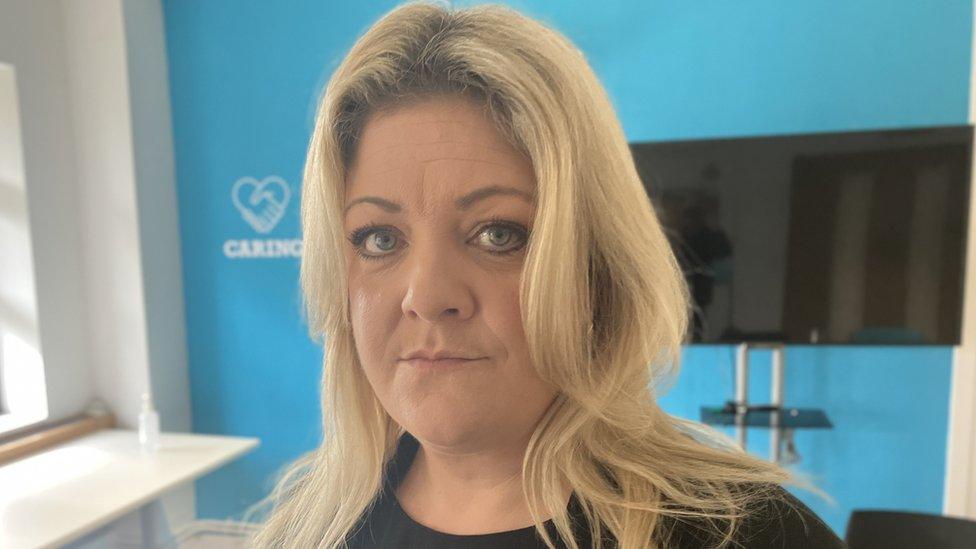 Picture of blonde women stood in blue-coloured room with a serious face looking at the camera