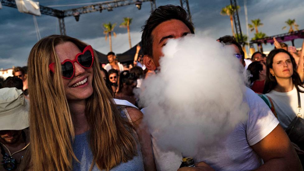 A festival-goer puffs a cloud of smoke from an electronic cigarette standing in a crowd of festival-goers in Cannes, south-eastern France, on 4 August 2023