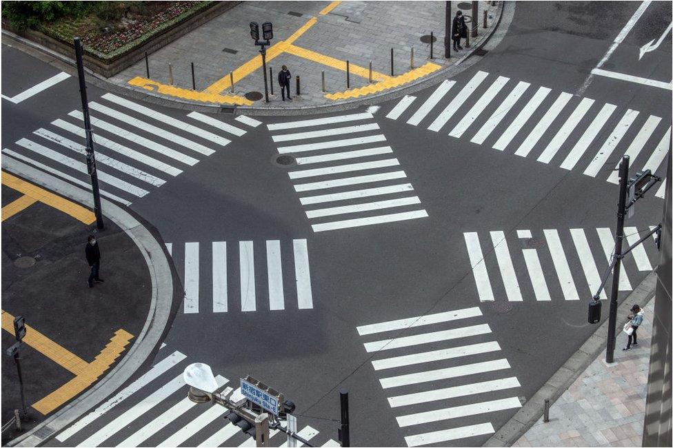 People wait to walk over a pedestrian crossing in Shinjuku during a nationwide a state of emergency in which many shops, restaurants, cafes and businesses have closed, on April 28, 2020 in Tokyo, Japan.