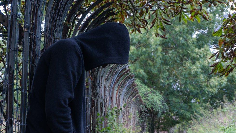 person in a hoodie leaning on a fence