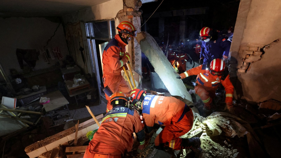 Rescuers in orange outfits climb through damaged buildings in Kangdiao village in Jishishan county